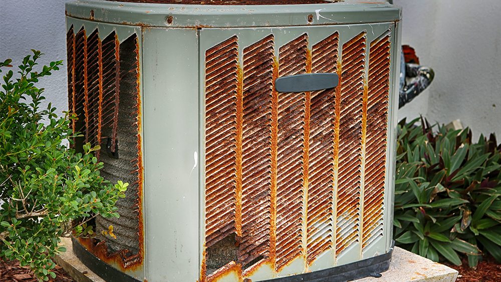 Aging rusted air conditioner condenser beside a home
